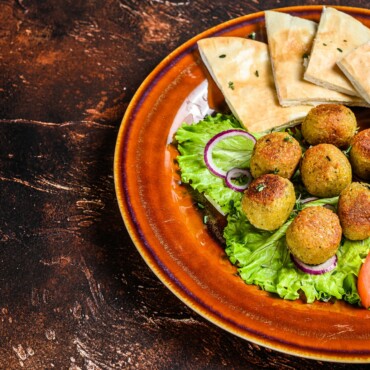 Vegetarian falafel with pita bread, fresh vegetables and sauce on a plate. Dark background